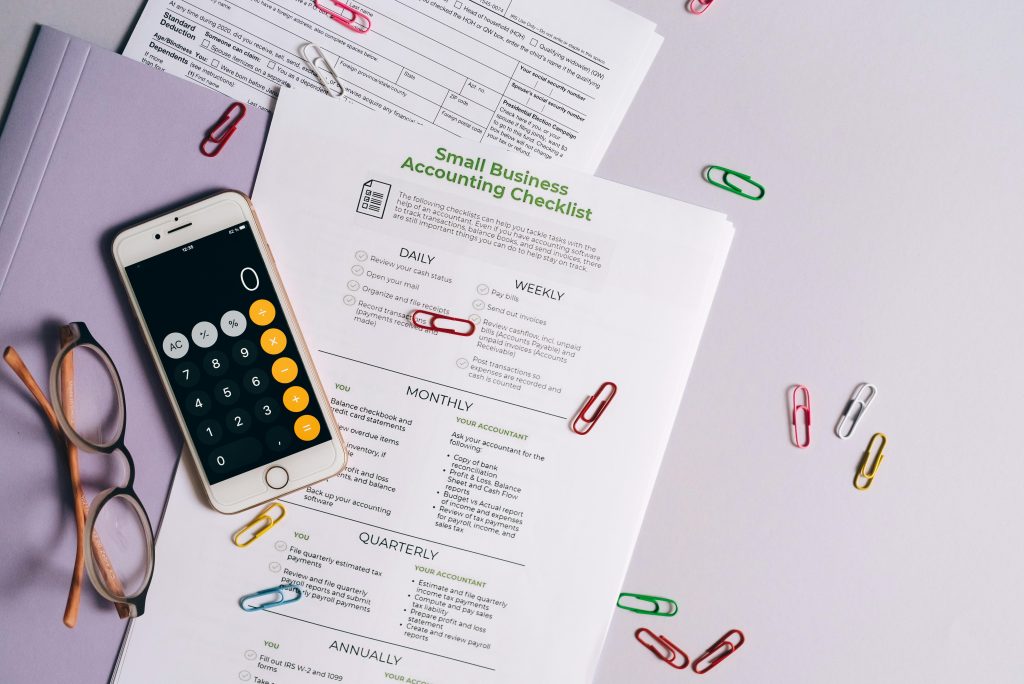 Small business accounting checklist with calculator, paperwork, and glasses - tools for auditing business finances and cutting unnecessary costs.